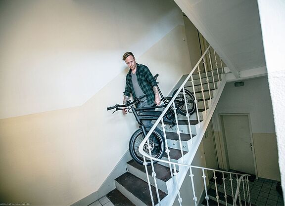 Fahrrad im Treppenhaus Ein Mann trägt ein Fahrrad in einem Treppenhaus.